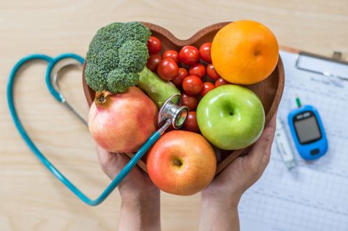 diabetic friendly foods: Image of hands holding a bowl of fruits with a blood glucose monitor and stethoscope in the background.