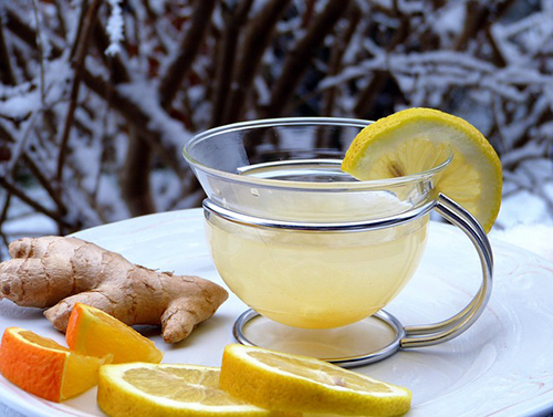 cup of lemon tea with lemon garnish, ginger, sliced oranges and lemons all representing a foods for a strong immune system