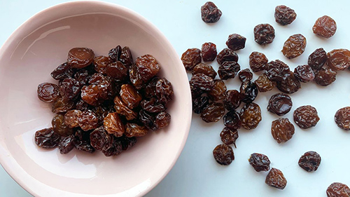 white bowl half full of raisins with some on the table next to the bowl