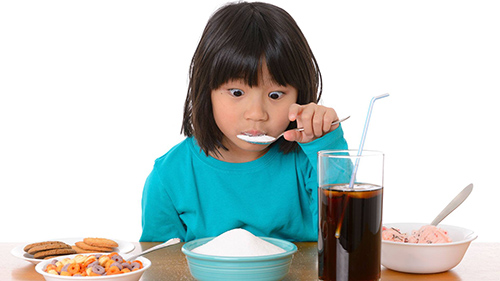 child eating a plate of sugar with all types of sugary snacks and drinks on the table