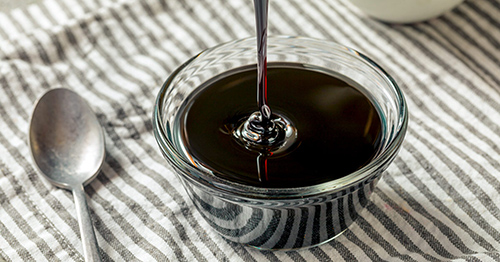 blackstrap molasses being poured into a small glass bowl with a spoon next to the glass on a tabel