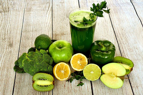 glass of green juice surrounded by all the green fruits and vegetables used to make it.