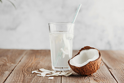 glass of coconut water with a straw and half open coconut on a table