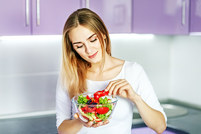 woman eating from a bowl filled with various vegetables