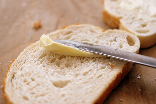 Foods that cause heart disease: Image of margarine being spread on a slice of bread using a butter knife