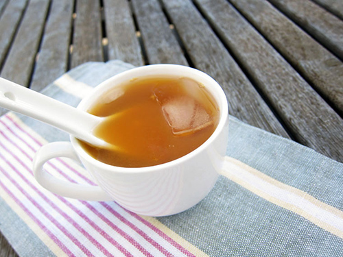 Cup of loquat tea on a table with a cube of inside for quicker cooling