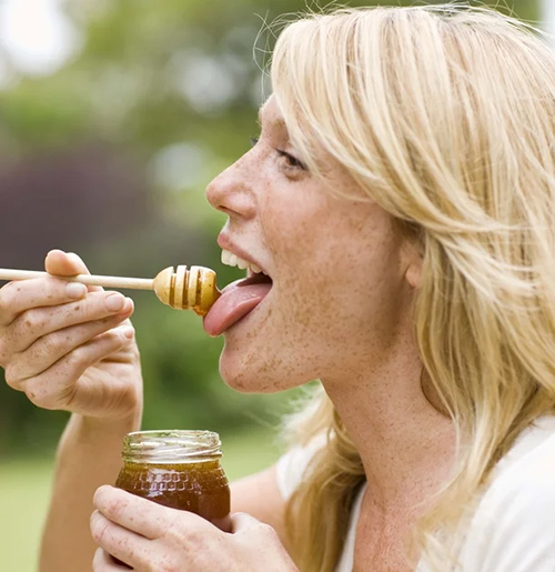 woman preparing to eat honey off of a honey comb while holding a jar of honey in her hand