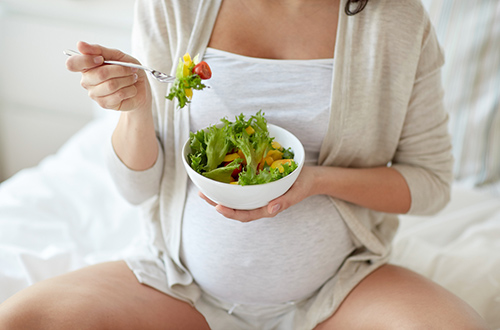 pregnant woman eating a bowl of green leafy vegetables