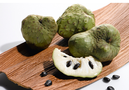 Three whole cherimoya fruits and one sliced on a cutting board
