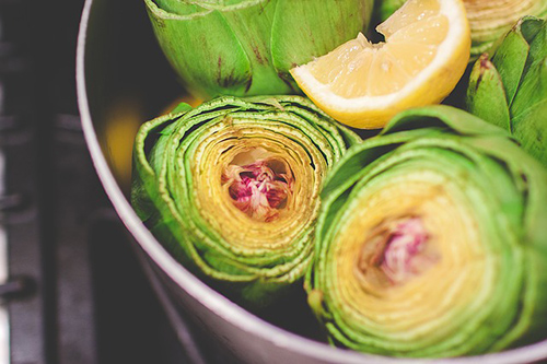 artichokes in a bowl and one is cut in half