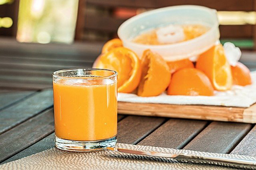 A glass of orange juice with sliced oranges on a cutting board in the background