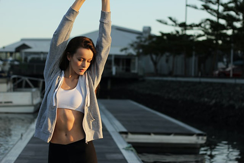 woman stretching with her arms raised above her head just before a morning jog
