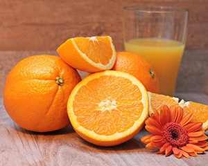 Tree oranges with one cut in half and a half glass of orange juice in the background