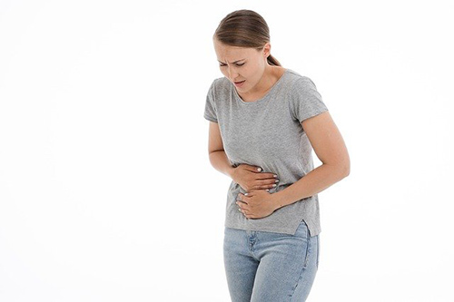 Woman keeled over in pain holding her stomach with both hands due to diverticulosis pain