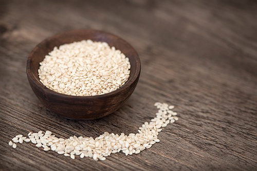 Bowl full of sesame seeds and overflow on the table