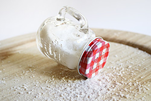 bottle of salt tipped over with salt overflow on the table