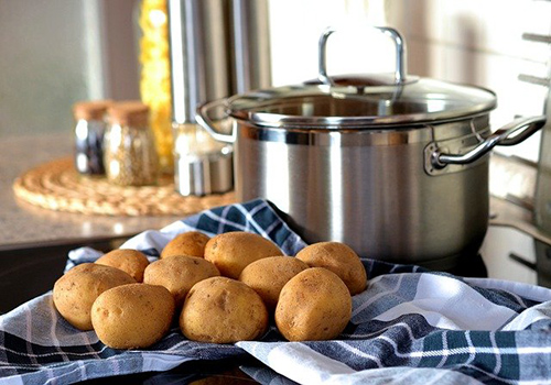 About a dozen potatoes on a table with a pot in the background