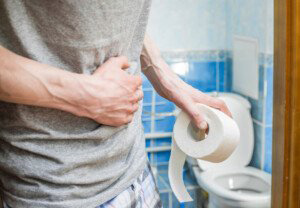 man holding a roll of toilet paper while holding his stomach and a toilet in the background