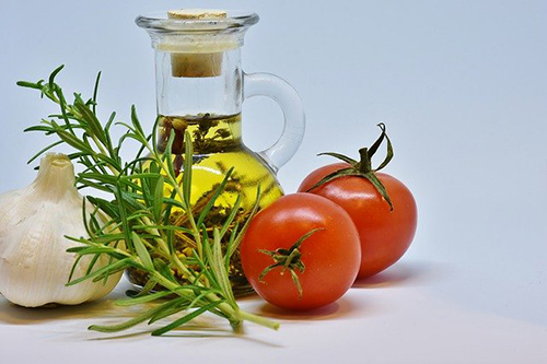 vegetable oil in glass container surrounded by tomatoes, garlic, and another herb