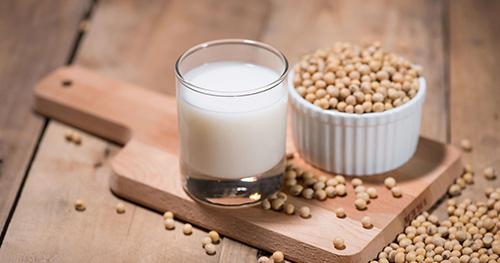 Glass of soymilk and a bowl of soybeans on a cutting board with soybean overflow on the table