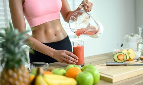 incredible fit woman pouring juice into glass surrounded by multiple fruits and vegetables she used for juicing for weight loss