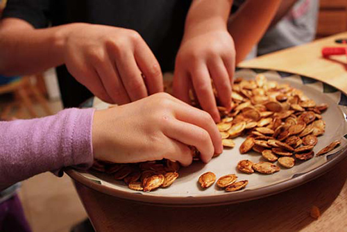 people reaching for pumpkin seeds in a bowl