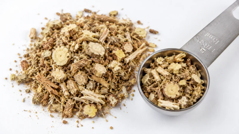 Cut and sifted dried marshmallow root on a white surface beside a measuring spoon.