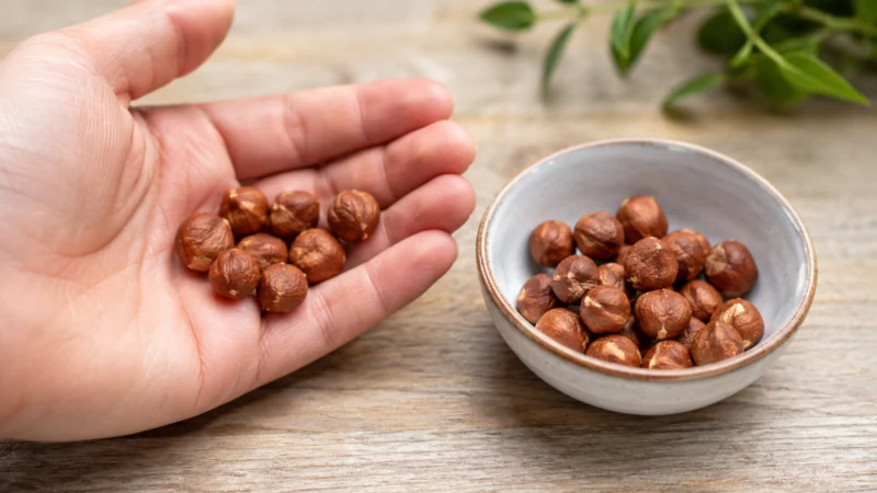 One-ounce serving of hazelnuts shown in a hand and a small bowl