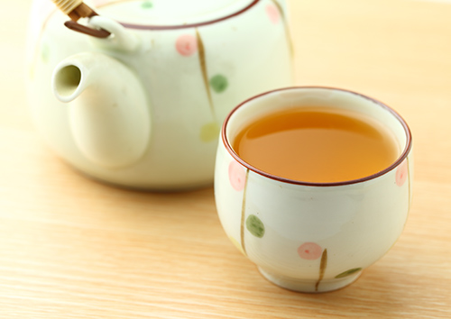 cup of orthosiphon tea with tea pot in the background