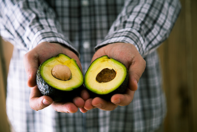 both hands of a man holding an avocado split in half