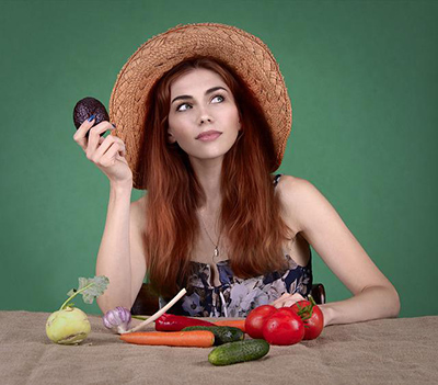woman sitting at a table in front of a variety of fruits and vegetables.