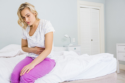 woman sitting on edge of the bed suffering from stomach disorders