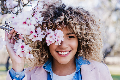 Almond health benefits: woman smiling with a branch with almond blossoms covering one of her eyes