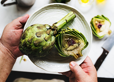 two hands holding plate with two artichokes on it about to put it on a table