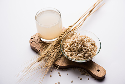 glass of barley water next to a bowl of barley grains