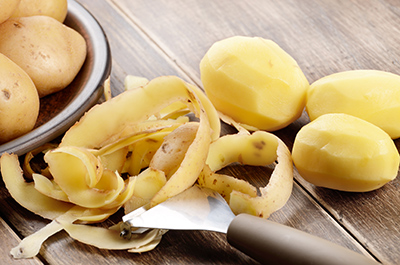 three peeled potatoes with the skin next to them