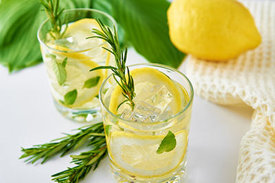 two glasses filled with water and lemon slices on a table with a whole lemon in the background