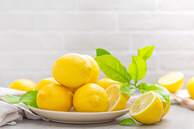 multiple whole lemons and one sliced lemon on a plate