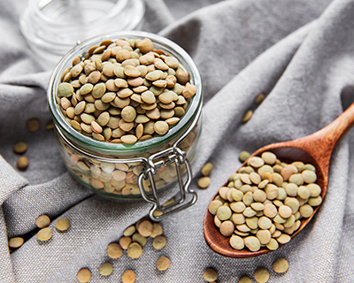 jar of overflowing lentils with a spoon filled with lentils next to it