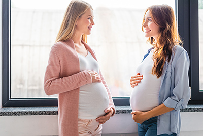 two pregnant women facing each other holding their stomachs