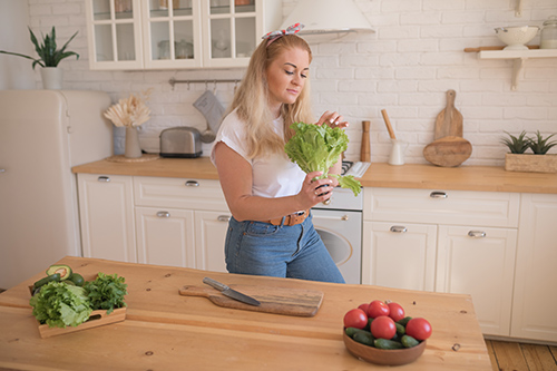 woman with a stalk of lettuce in the kitchen: health benefits of lettuce