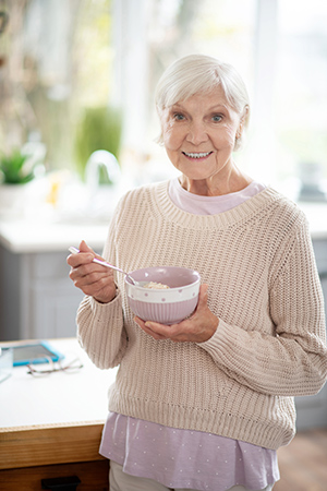 woman standing in her kitchen holding a bowl of oatmeal with a spoon