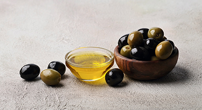 green and block olives in a wooden bowl next to tiny glass bowl of olive oil