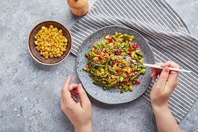 hands with a fork about with a plate of peas and corn on a table