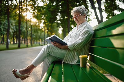 older woman sitting on park bench reading a book