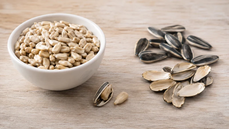 Shelled sunflower kernels in a bowl beside striped sunflower seeds and discarded hulls