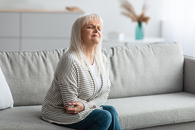 older woman sitting on the couch holding her stomach in pain