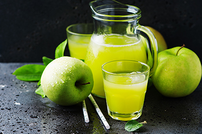 green apples with a mug and a glass filled with apple juice