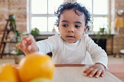 baby reaching for orange on a table