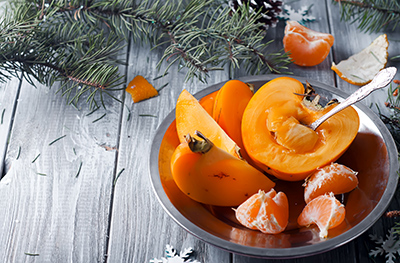 sliced ripe persimmon with 3 cloves of tangerine in a bowl